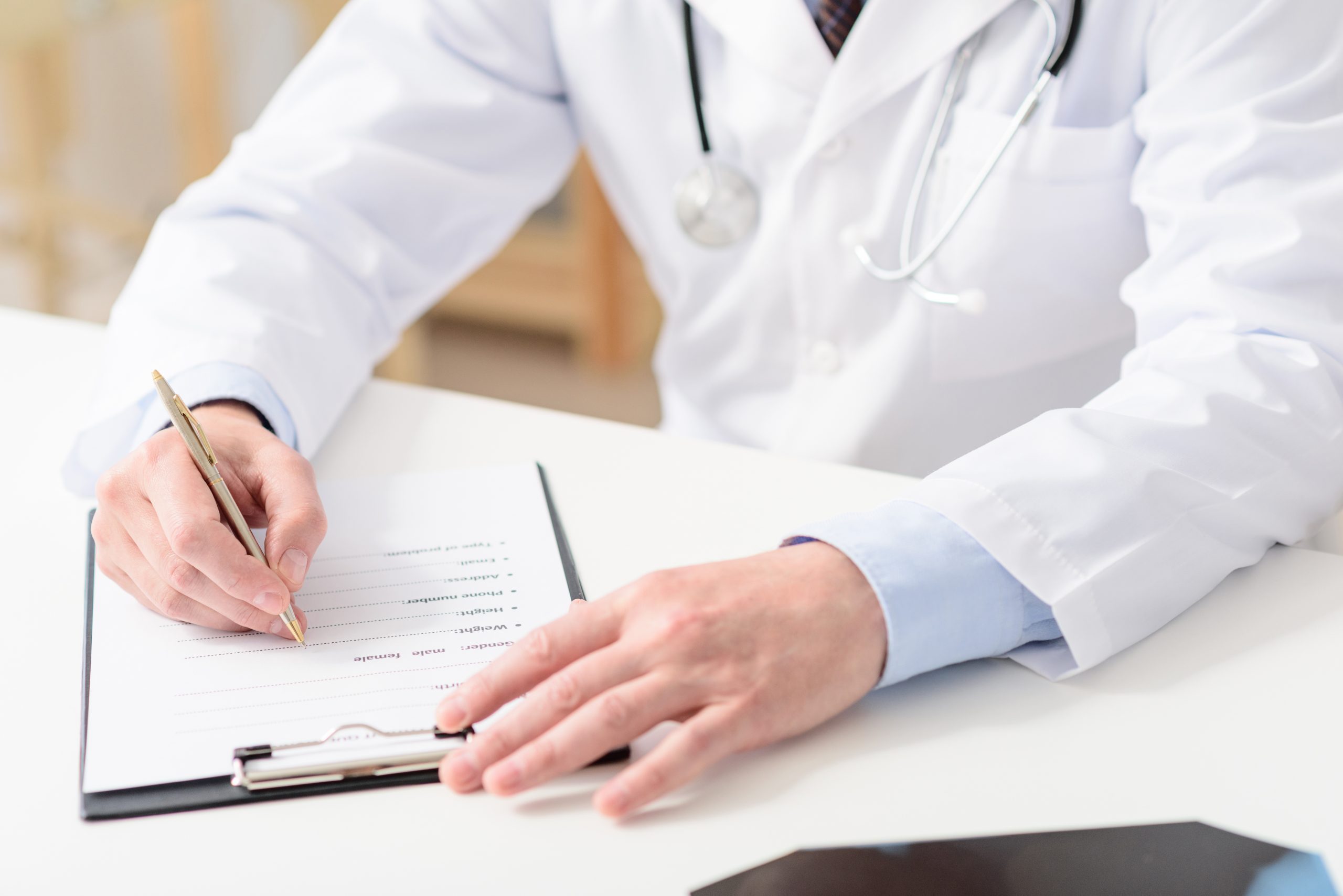 Accessing medical records. Close up of doctor writing on his clipboard, sitting in his office